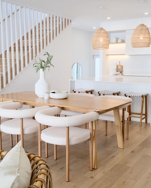 a dining room table with white chairs and stools in front of the staircase leading to an open floor plan