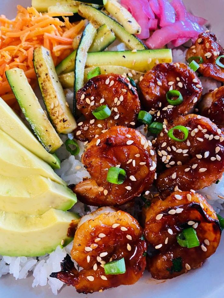 a white plate topped with shrimp, avocado and rice covered in sesame seeds