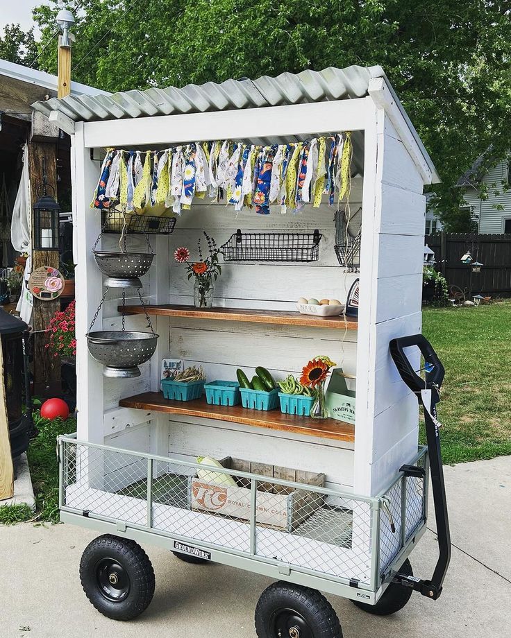 an outdoor garden cart with plants and pots on the shelves, in front of a house