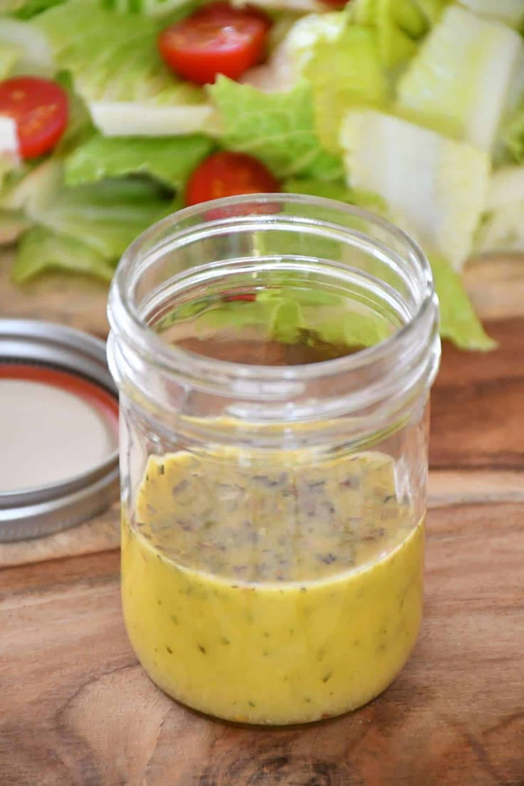 a jar filled with dressing sitting on top of a wooden cutting board next to a salad