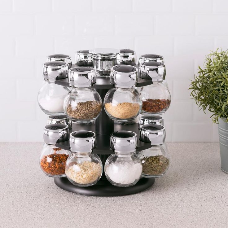 an assortment of spices and seasonings in glass jars on a black stand next to a potted plant