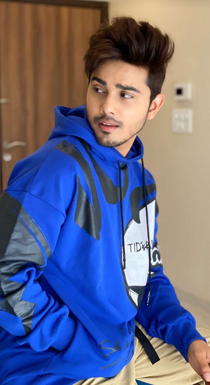 a young man in a blue hoodie sitting on top of a wooden table next to a door