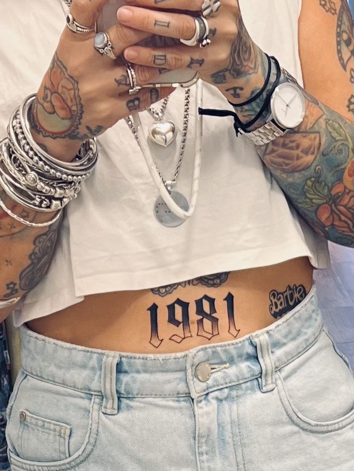 a person with tattoos on their stomach holding a cell phone and looking at the camera