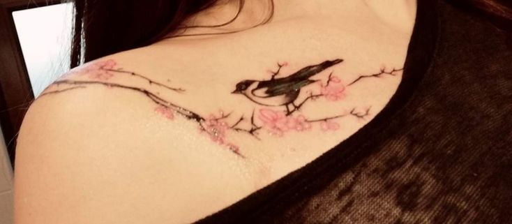 a woman's shoulder with a bird on the branch and pink flowers around it