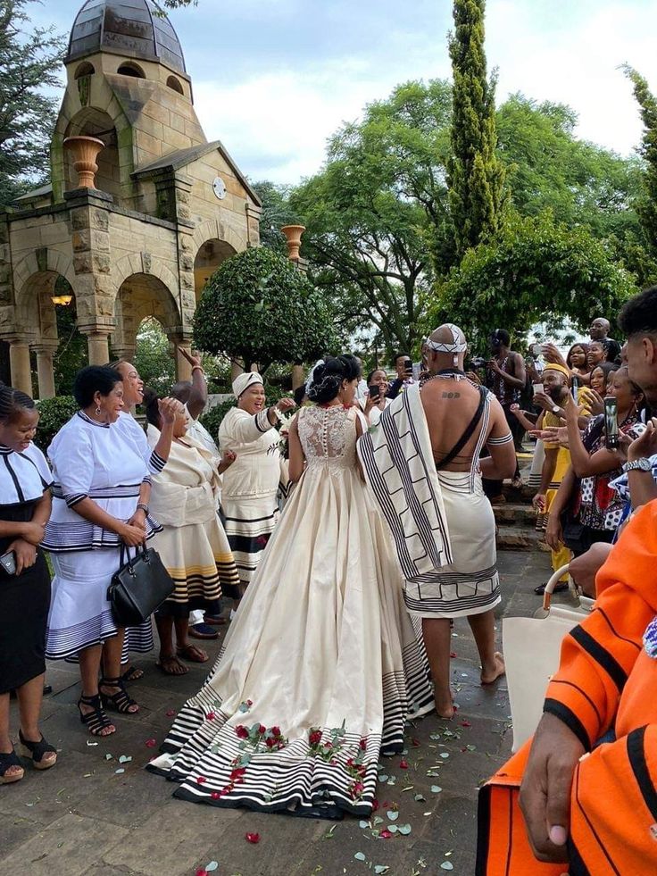 a group of people standing around each other in front of a building with flowers on the ground