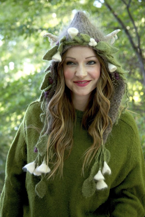 a woman wearing a green hoodie with white flowers on her head and ears is standing in the woods