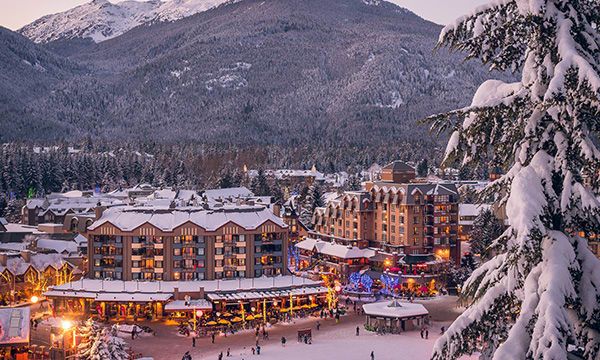 the town is surrounded by snow covered mountains and evergreen trees with lights on them at night