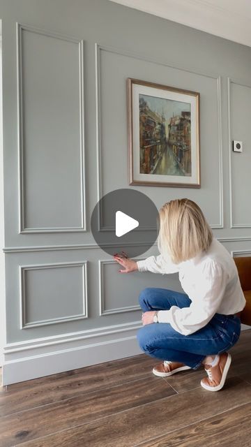 a woman kneeling down on the floor in front of a wall with a painting hanging above it