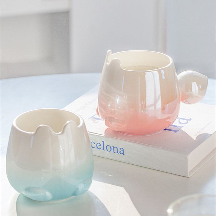 two cups sitting on top of a white table next to a book and glassware