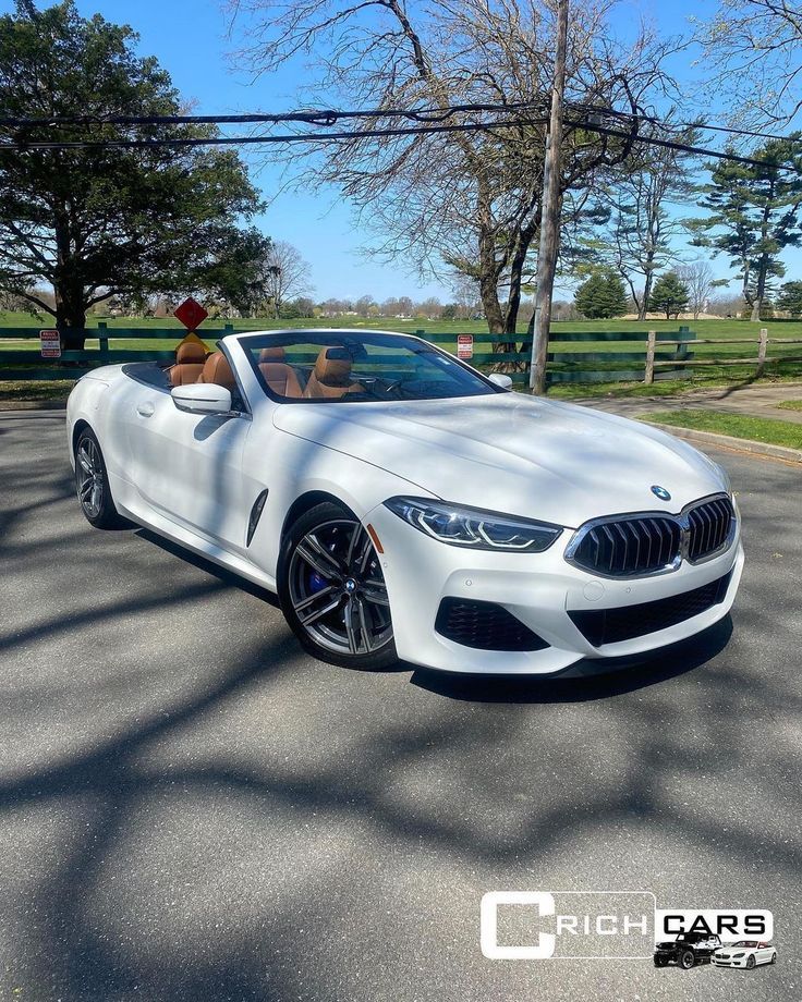 a white bmw z4 convertible parked in a parking lot with trees and grass behind it