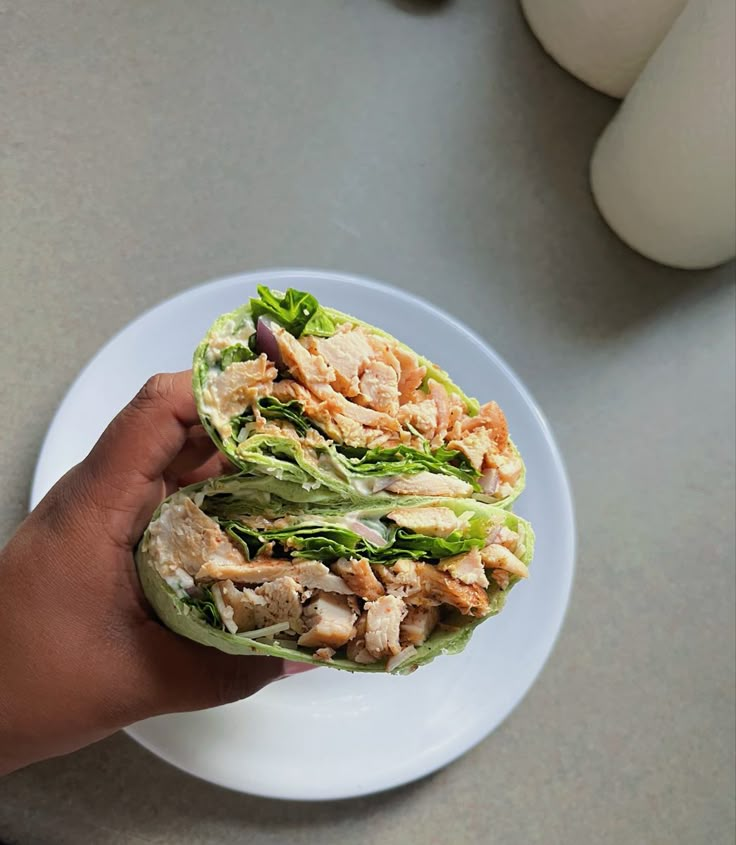 a hand holding a half eaten chicken and lettuce sandwich on a white plate