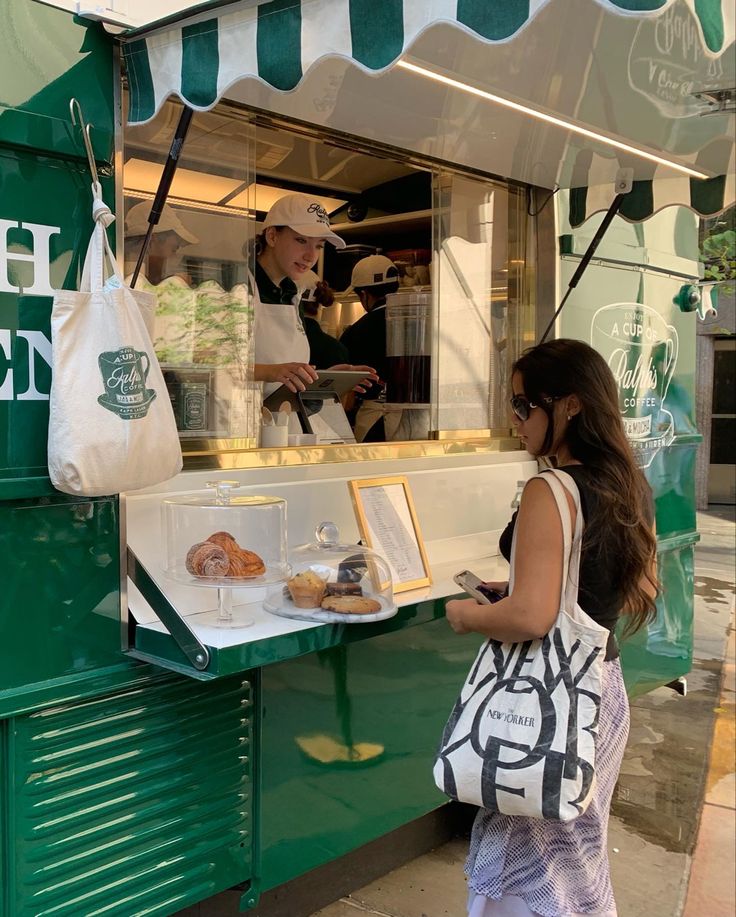 a woman standing in front of a green food truck with a man behind the counter