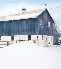 a blue and white barn sitting in the middle of a snow covered field next to a fence