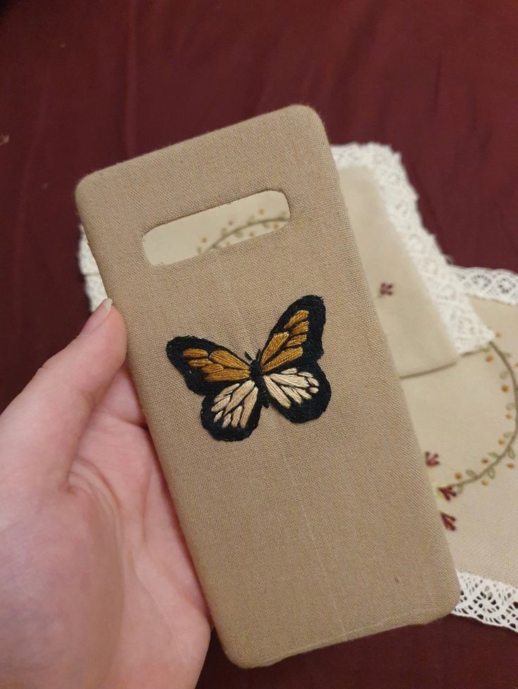 a hand holding a cell phone case with a butterfly applique on it