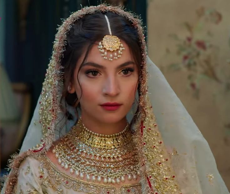 a woman wearing a bridal outfit with gold jewelry on her head and veil over her face