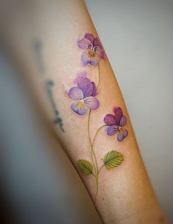 a woman's arm with purple flowers and green leaves on the left side of her arm