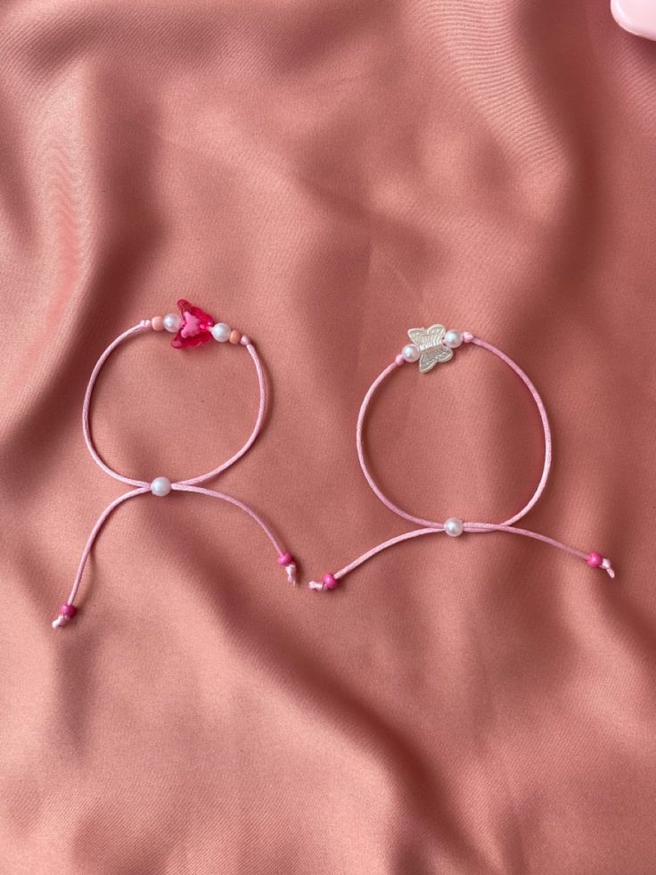 two pink bracelets laying on top of a pink satin bed sheet with beads and charms