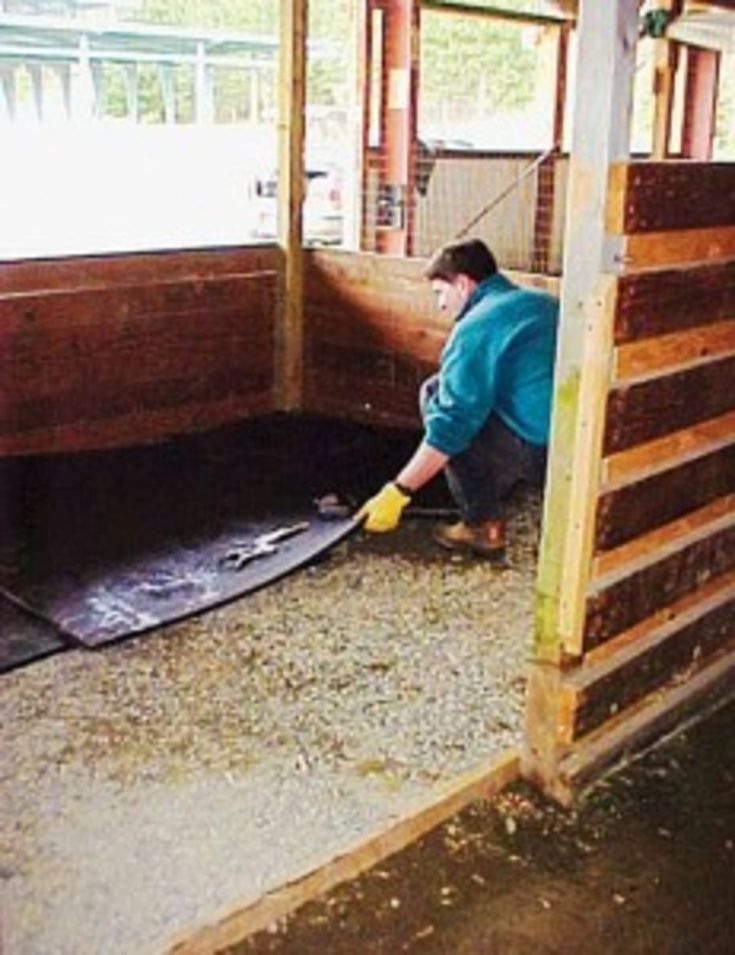 a man in blue shirt and yellow gloves working on an animal pen with wooden walls