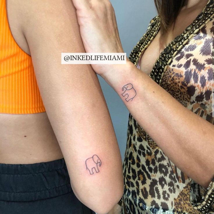 two women with matching tattoos on their arms, one is holding the other's arm