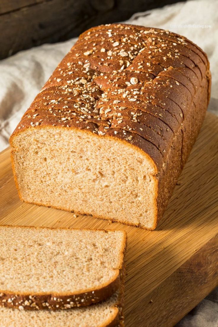 a loaf of bread sitting on top of a wooden cutting board next to a slice of bread