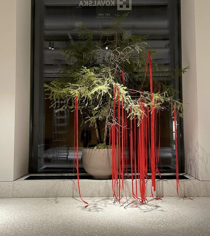 a potted plant with red ribbons hanging from it's sides in front of a building