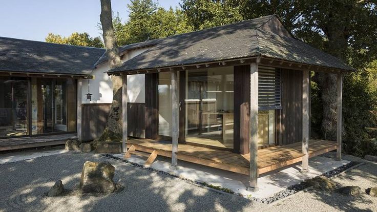 a small wooden building sitting on top of a gravel field next to trees and rocks