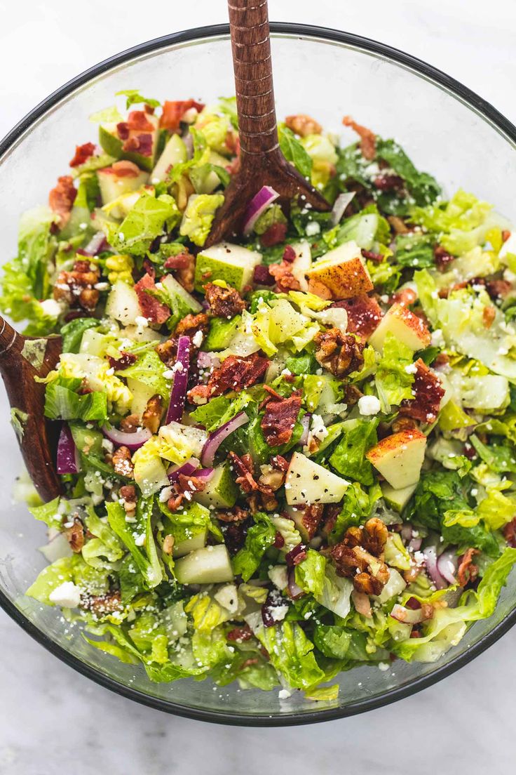 a salad in a glass bowl with a wooden spoon