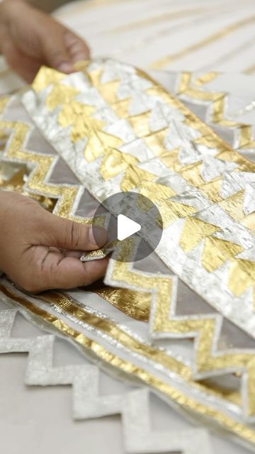 a person is working on some gold and silver fabric with their hand over the edge