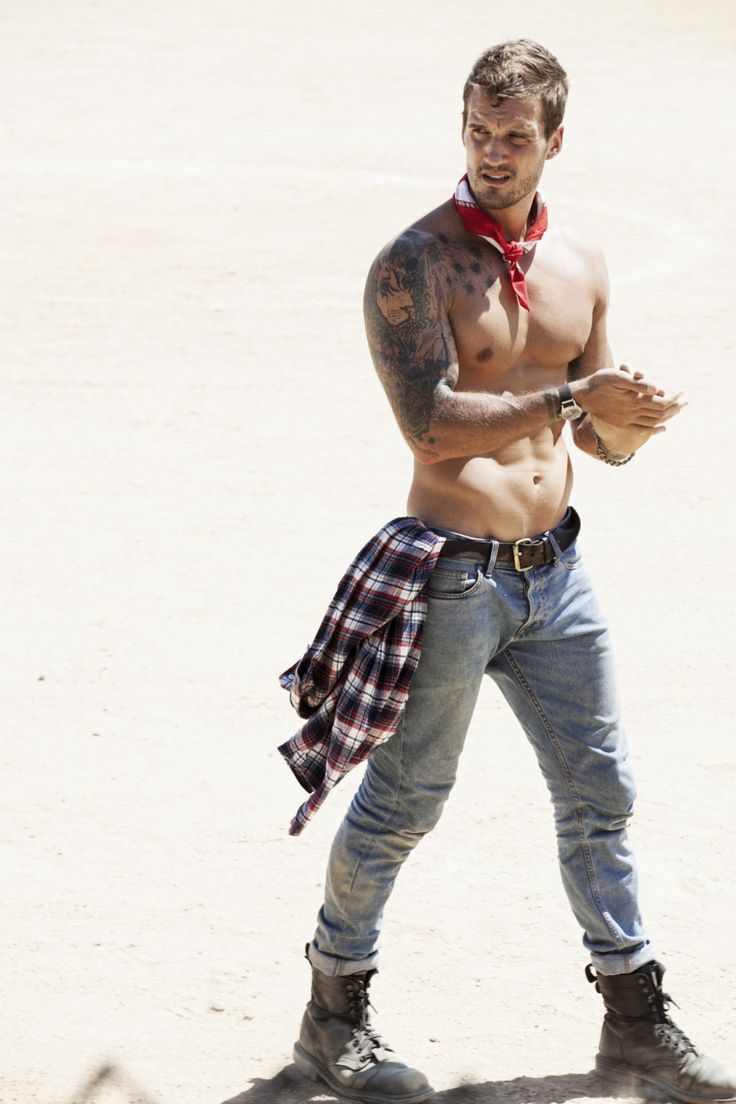 a shirtless man holding a baseball in his right hand while standing on the sand