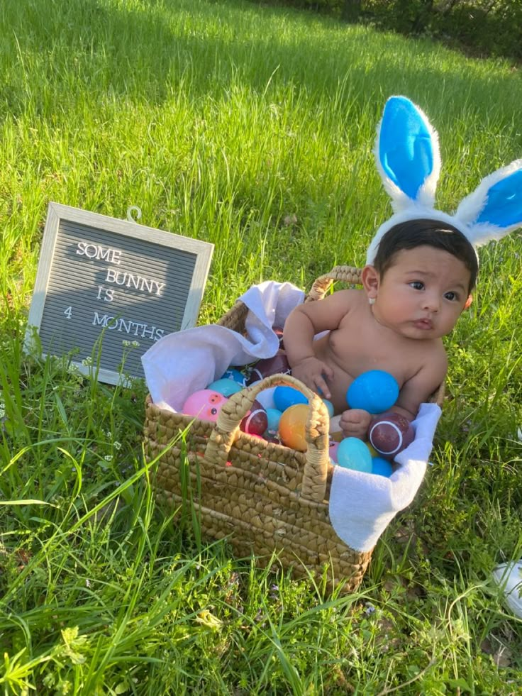 a baby wearing bunny ears sitting in a basket next to an easter egg hunt sign