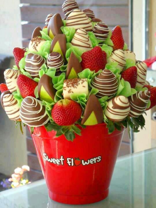 a red bucket filled with chocolate covered strawberries and topped with green leafy leaves