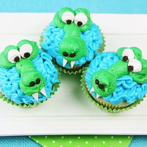 four cupcakes with blue frosting and green icing decorated like crocodiles