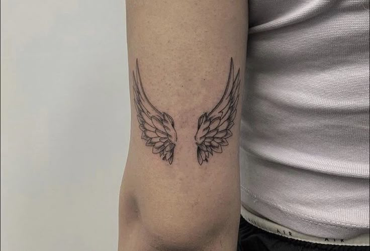 a woman's arm with an angel wing tattoo on the left side of her arm