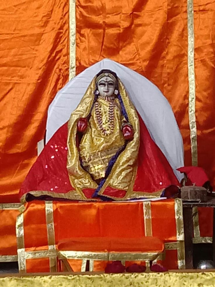 the statue is sitting in front of an orange cloth covered stage with gold trimmings