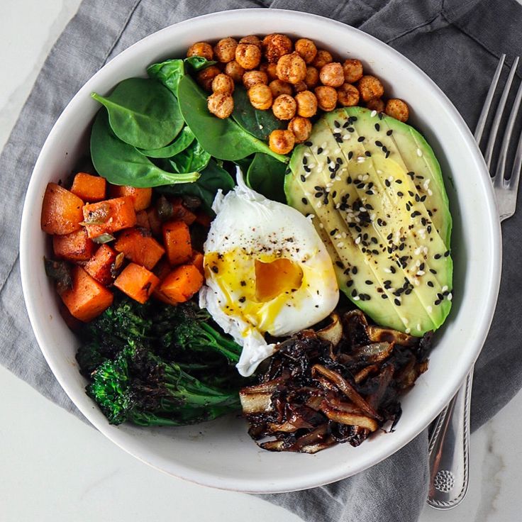 a white bowl filled with vegetables, eggs and meats on top of a gray napkin