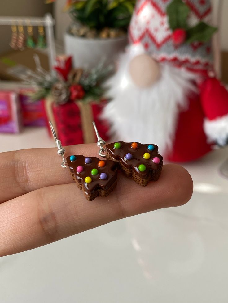 a hand holding two pieces of chocolate with candy on them and santa's hat in the background