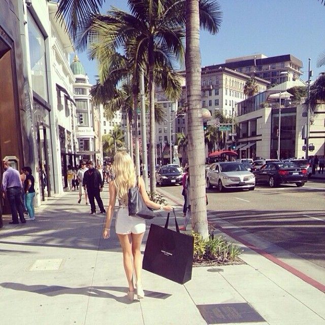 a woman is walking down the street with her shopping bags in hand and palm trees lining the sidewalk