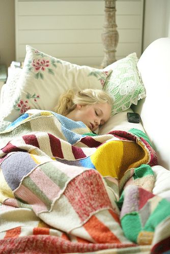 a woman laying in bed under a blanket with her head resting on the end of the pillow