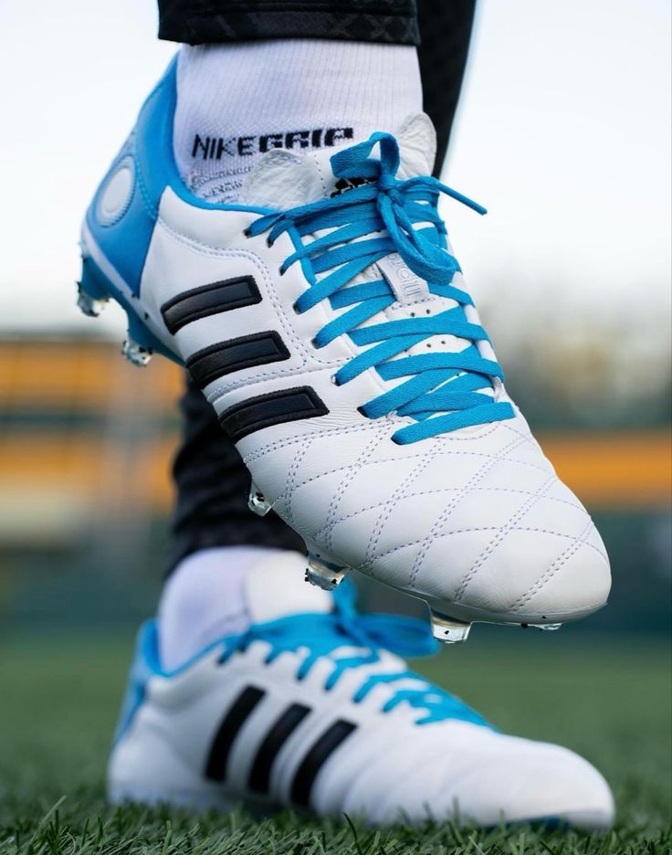 the feet of a soccer player wearing white and blue shoes with black stripes on them