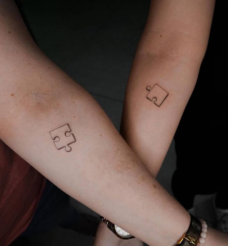 two people with matching tattoos on their arms holding each other's hands and one has the word puzzle written on it