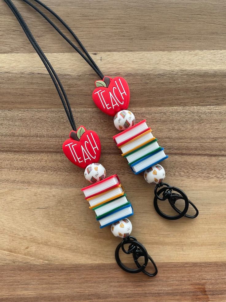 two necklaces made out of books and apple charms with the words teach written on them