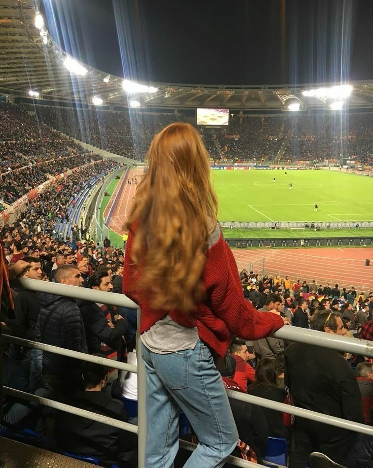 a woman standing in front of a crowd at a soccer game looking over the bleachers