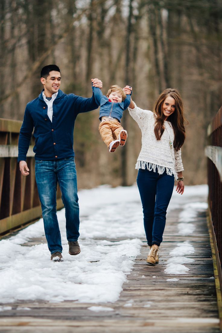 a man and woman walking across a snow covered bridge with a baby in their arms