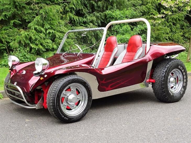 a red and silver dune buggy is parked on the side of the road in front of some trees