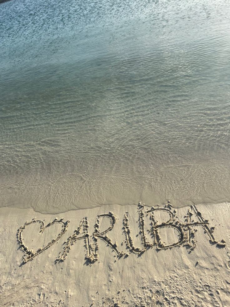 the word aruba written in sand at the beach with water and sky behind it