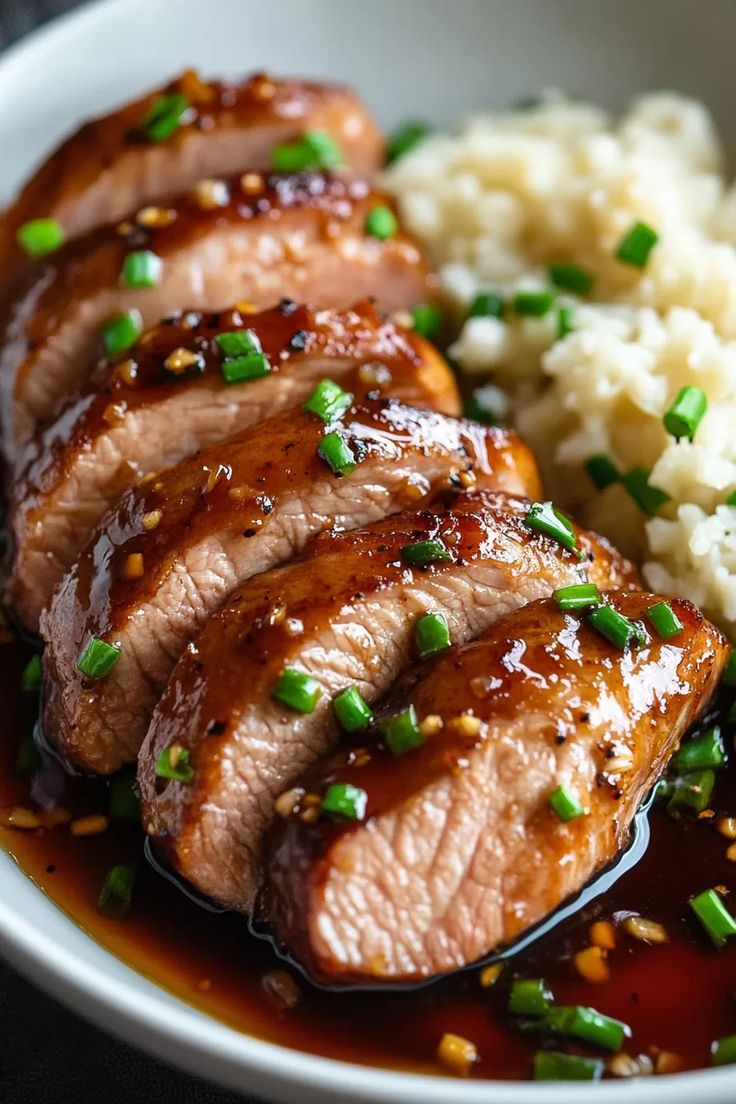 some meat and rice in a white bowl with green onions on the side for garnish