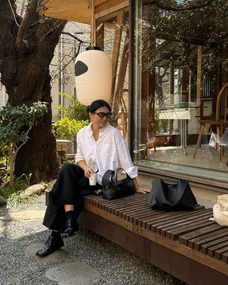 a woman sitting on a bench in front of a store window holding her purses