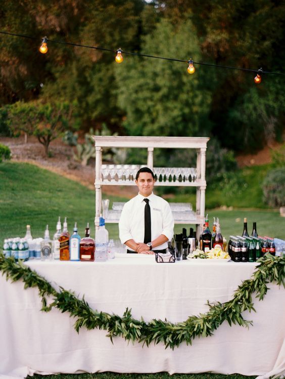 a man sitting at a table with bottles and glasses on it in front of an outdoor bar