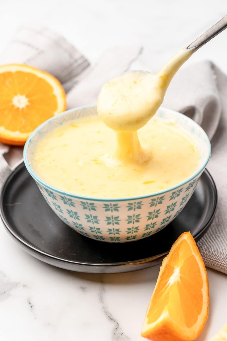 an orange being drizzled with dressing in a blue and white bowl on a black plate