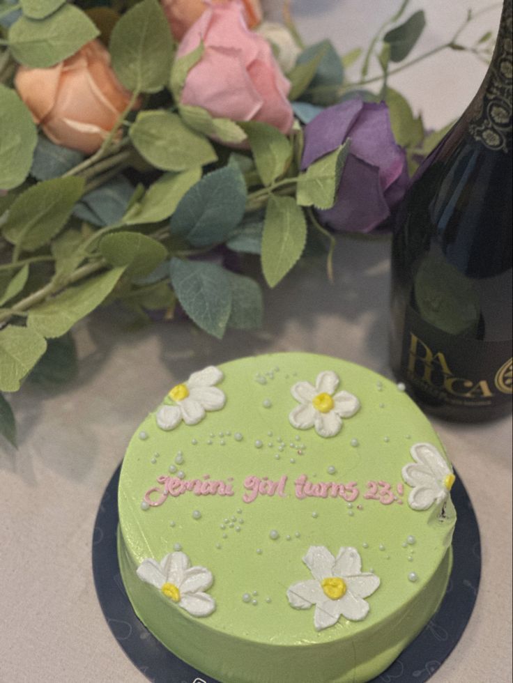 a green cake sitting on top of a table next to flowers and a wine bottle